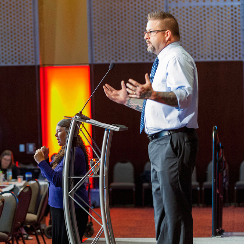 Image of Kevin Gannon delivering a lecture at a podium in front of a screen