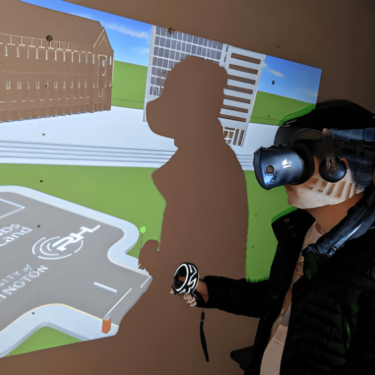 Person stands with VR goggles on and there is a projected screen